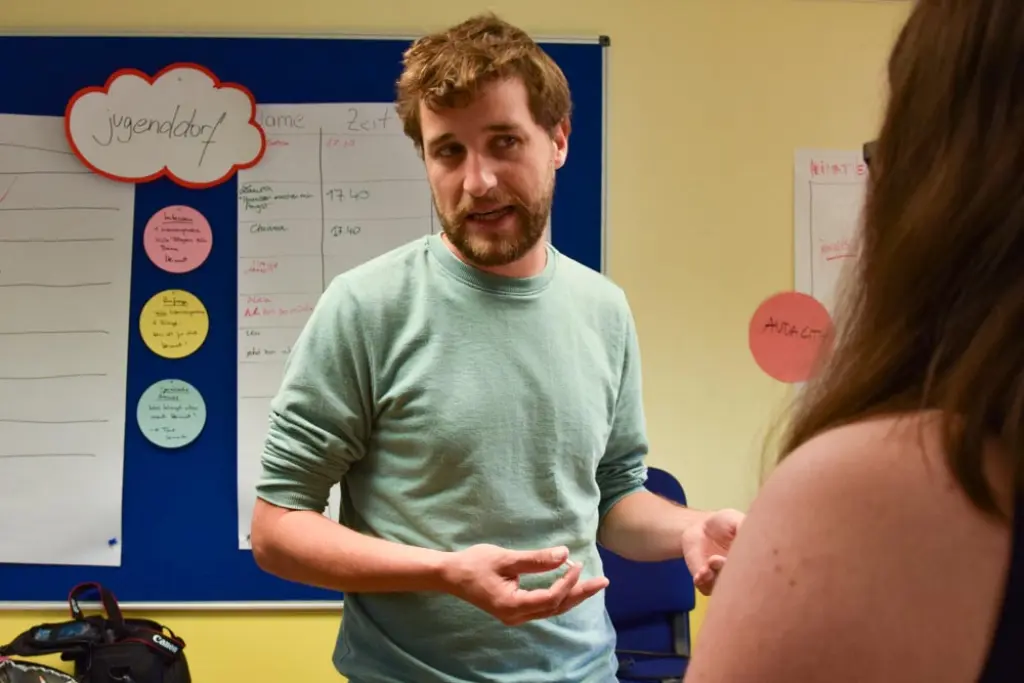 Torsten Fischer steht gestikulierend vor einer Tafel mit Plakaten.