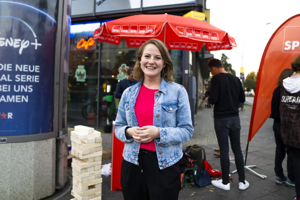Annika Klose steht vor ihrem Wahlkampfstand. Links sieht man eine Litfaßsäule, im Hintergrund ein Café.