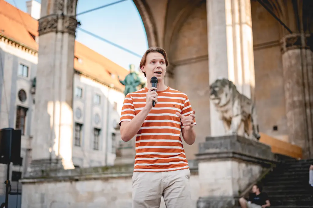 Kai Fackler steht mit einem Mikrofon vor einem Gebäude.