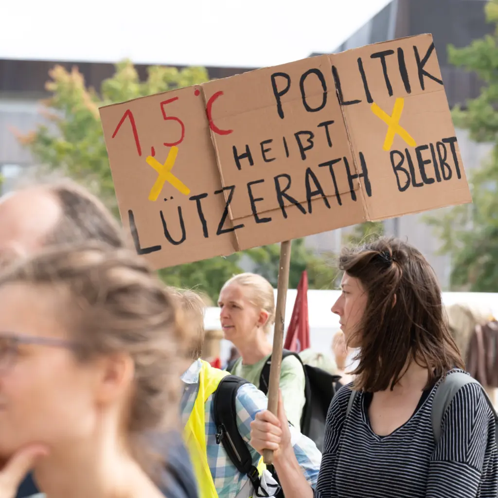 FridaysForFuture-Demonstrant*innen. Eine Demonstrantin hält ein Pappschild mit der Aufschrift: 1,5-Grad-Politik heißt Lützenrath bleibt.