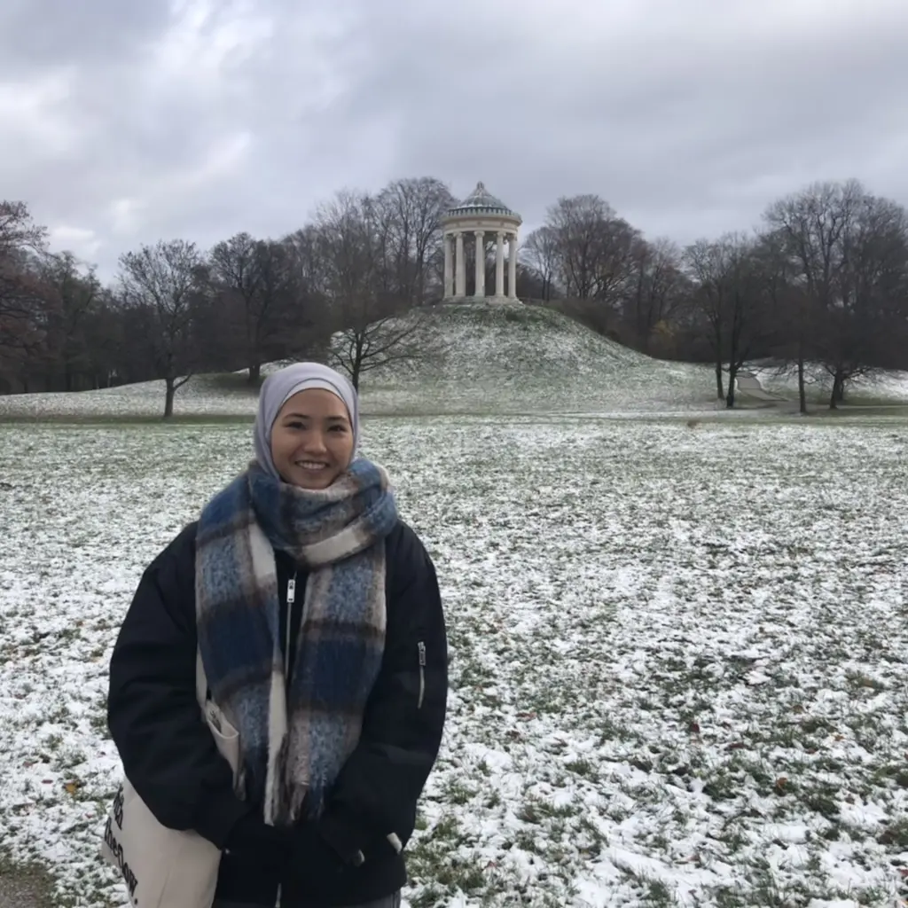 Zohra steht lächend im Englischen Garten in München, Deutschland.