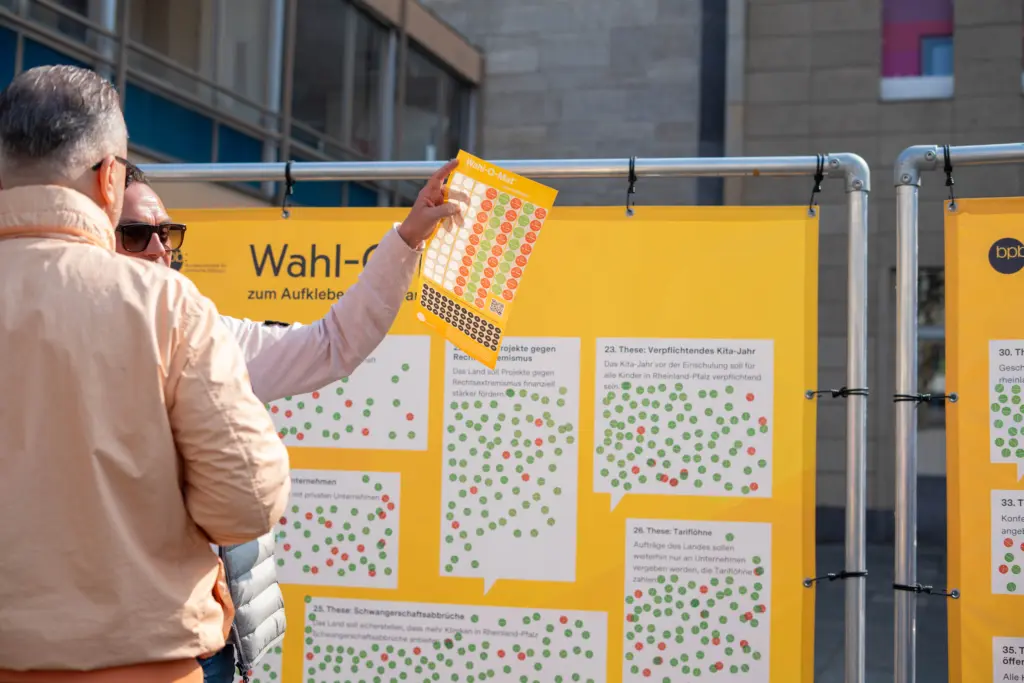 Menschen unterhalten sich beim Bestickern des analogen Wahlo-O-Mat.